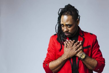 Kapalı stüdyo portresi. Kırmızı ceketli bir adam. İki eli de kalpte.