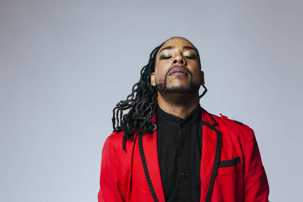 Студийный портрет человека в красном пиджаке и дредах
