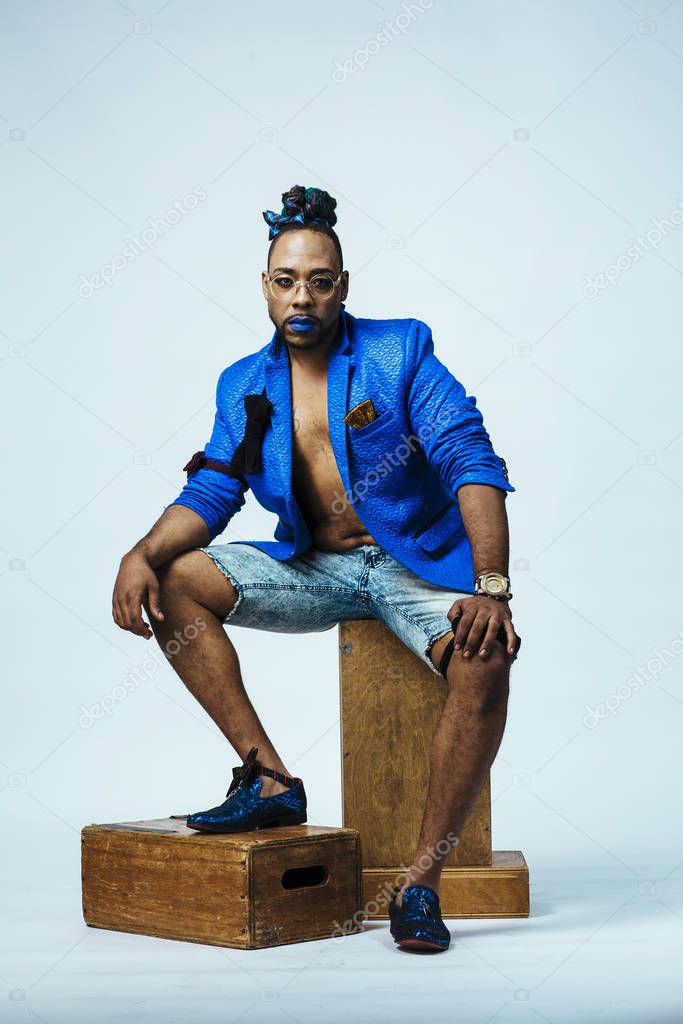 Studio portrait of a man with blue outfit and blue lips sitting
