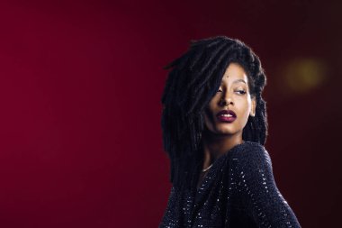 Stüdyo portresi. Rastalı bir kadın. Stüdyoda kırmızı arka planda parlak bir elbise giyiyor.