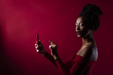 Stüdyo portresi, kırmızı arka planlı bir stüdyo resminde ışıltılı bir elbise giyen rastalı bir kadının. Cep telefonundan mesaj atıyor.