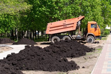 car dumper unloads the black earth on the flowerbed in city park clipart