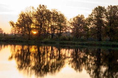  Manzara. Gölün üzerinde gün batımı, suya yansıyan düşen ağaçlar..