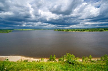 Yaz manzarası, büyük bir nehir, nehrin kıyısında çayır çiçekleri, gökyüzünde güçlü bulutlar, Kama Nehri boyunca bir turist yürüyüşü.