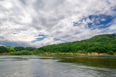 Yaz fotoğrafı, güçlü gök gürültülü bulutlar, mavi gökyüzü, karanlık keskin su, Kama Nehri boyunca turist yürüyüşü.