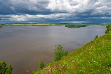 Yaz manzarası, büyük bir nehir, nehrin kıyısında çayır çiçekleri, gökyüzünde güçlü bulutlar, Kama Nehri boyunca bir turist yürüyüşü.
