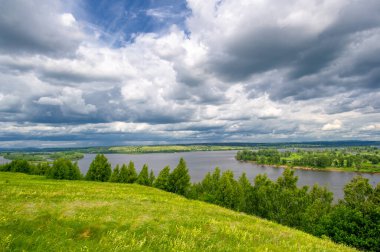 Yaz manzarası, büyük bir nehir, nehrin kıyısında çayır çiçekleri, gökyüzünde güçlü bulutlar, Kama Nehri boyunca bir turist yürüyüşü.