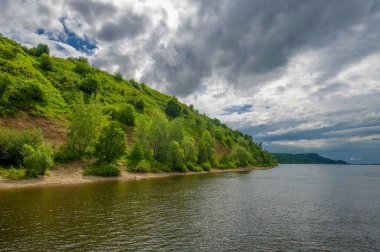 Yaz fotoğrafı, güçlü gök gürültülü bulutlar, mavi gökyüzü, karanlık keskin su, Kama Nehri boyunca turist yürüyüşü.
