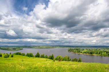 Yaz manzarası, büyük bir nehir, nehrin kıyısında çayır çiçekleri, gökyüzünde güçlü bulutlar, Kama Nehri boyunca bir turist yürüyüşü.