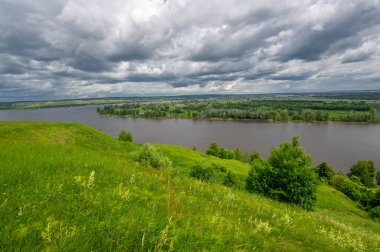Yaz manzarası, büyük bir nehir, nehrin kıyısında çayır çiçekleri, gökyüzünde güçlü bulutlar, Kama Nehri boyunca bir turist yürüyüşü.