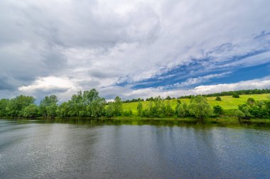 Yaz fotoğrafı, güçlü gök gürültülü bulutlar, mavi gökyüzü, karanlık keskin su, Kama Nehri boyunca turist yürüyüşü.