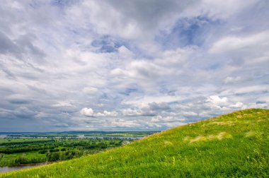 Yaz manzarası, büyük bir nehir, nehrin kıyısında çayır çiçekleri, gökyüzünde güçlü bulutlar, Kama Nehri boyunca bir turist yürüyüşü.
