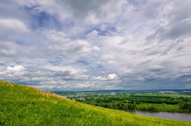 Yaz manzarası, büyük bir nehir, nehrin kıyısında çayır çiçekleri, gökyüzünde güçlü bulutlar, Kama Nehri boyunca bir turist yürüyüşü.