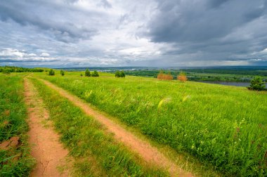 Yaz manzarası, büyük bir nehir, nehrin kıyısında çayır çiçekleri, gökyüzünde güçlü bulutlar, Kama Nehri boyunca bir turist yürüyüşü.