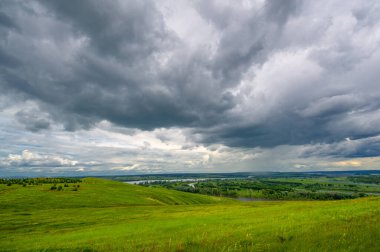Yaz manzarası, büyük bir nehir, nehrin kıyısında çayır çiçekleri, gökyüzünde güçlü bulutlar, Kama Nehri boyunca bir turist yürüyüşü.