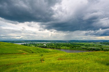 Yaz manzarası, büyük bir nehir, nehrin kıyısında çayır çiçekleri, gökyüzünde güçlü bulutlar, Kama Nehri boyunca bir turist yürüyüşü.