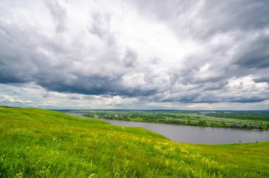 Yaz manzarası, büyük bir nehir, nehrin kıyısında çayır çiçekleri, gökyüzünde güçlü bulutlar, Kama Nehri boyunca bir turist yürüyüşü.