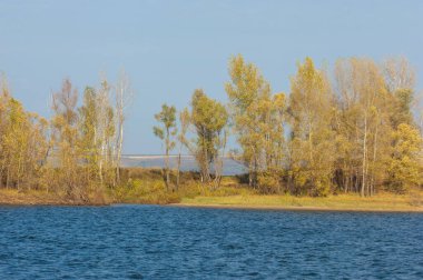 Sonbahar manzarası, koyu mavi su, son sıcak günler, nehir, ağaçlar, rüzgarlı hava, sarı-kırmızı sonbahar yaprakları.