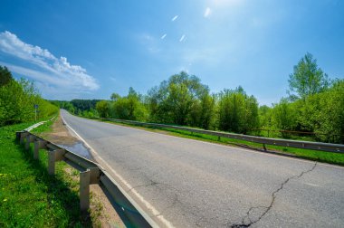 Geniş açılı mercek, yerel otoyol, parlak yeşil ağaçlar, mavi gökyüzündeki bulutlar...