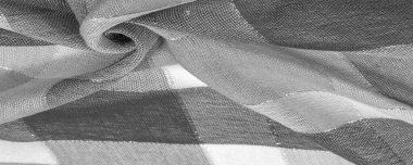 Doku, arkaplan, ipek atkı siyah beyaz, metal şeritli. Eşarp, soyut İskoç motifleriyle pastel renklerle hassas bir yama deseniyle süslenmiş. kontrol edilen kumaş