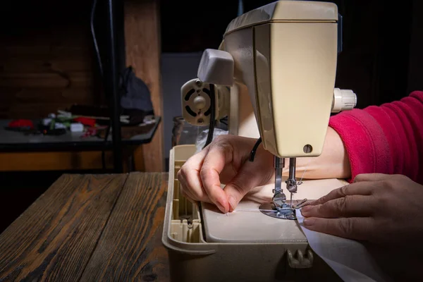 Frauenhände nähen in einer Werkstatt ein blaues Kleid an einer professionellen Overlock-Maschine. Näherin Hände, die Textilien zum Nähen von Kleidung halten. Unscharfe Nahaufnahme des Nähvorgangs im Hintergrund. — Stockfoto