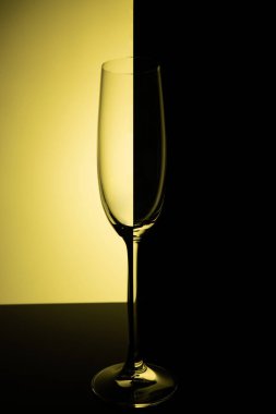 Empty champagne glass with reflection, on a yellow and black gradient background. Club life concept.