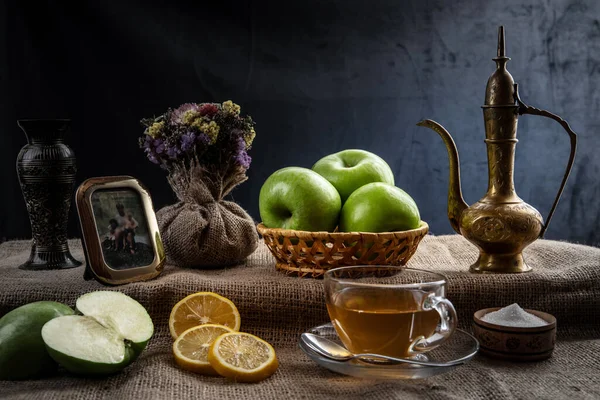 Natureza morta, chá da manhã com limões e maçãs em uma atmosfera caseira, em cores escuras com iluminação brilhante . — Fotografia de Stock