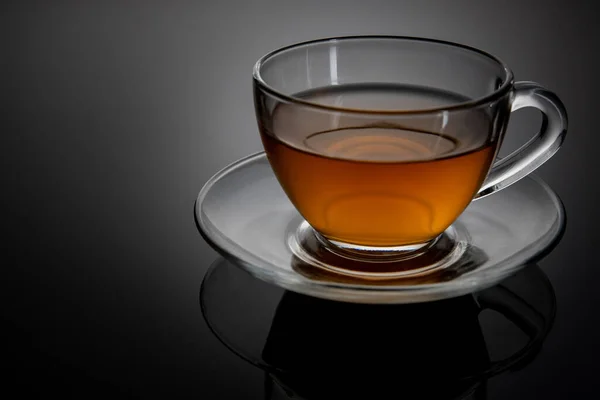 Glass cup of tea on a glass saucer with reflection, with a gradient of black and gray background. Concept, healthy and stylish lifestyle. — Stock Photo, Image