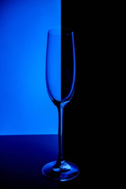 Empty champagne glass with reflection, on blue and black gradient background. Club life concept.