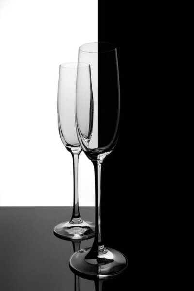 Two empty glasses of champagne with reflection, on a white and black gradient background. Club life concept.