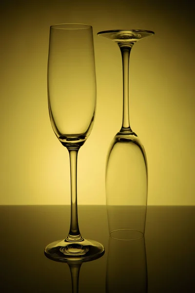 Dois copos vazios de champanhe com reflexão, em um fundo gradiente amarelo e preto. Conceito, festa e vida de clube . — Fotografia de Stock