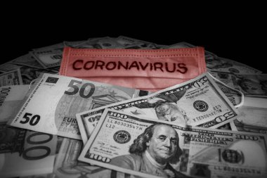 Coronavirus inscription on a medical mask on top of world international banknotes. US dollars and euros. Coronavirus Warning.
