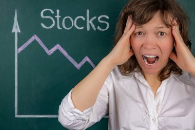 The concept of a business crisis, a young businesswoman clutching her head in horror, in the background is a stock chart with a negative trend.