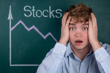 Concept business crisis, angry young businessman in horror clutching his head, in the background is a stock chart with a negative trend.