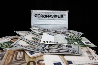 Coronavirus inscription on a medical mask on top of world international banknotes. US dollars and euros. Coronavirus Warning.