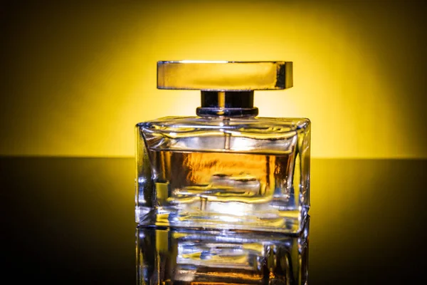 Perfume bottle in the rays of gray light on a black background. The play of light on a perfume bottle, can be used as a magazine and commercial photo with place for text or design