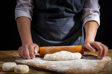 Female hands knead the dough on a wooden antique table on a dark background, close-up, shallow depth of field, beautiful directional lighting. Concept of home baking and comfort.