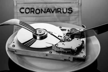 A medical mask with the inscription Coronavirus and a computer hard drive with a fork and knife, personifying the helplessness of modern technology in the fight against the virus.