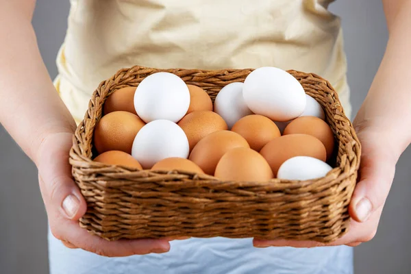 Female hands hold a basket of fresh chicken eggs, close-up, selective focus, shallow depth of field. The concept of healthy food, spring religious holidays. Stock Photo