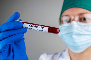 Coronavirus salgını, solunum maskeli bir hemşire COVID 19 etiketli bir test tüpü tutuyor, hızla yayılan yeni bir koronavirüs için pozitif kan testi, yakın plan, sığ alan derinliği, seçici