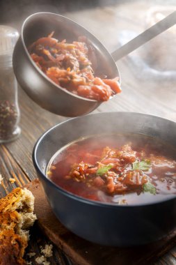 Borsch bir kepçeden bir kaseye dökülüyor, buhar, geleneksel bir Ukrayna sebze çorbası pancar, havuç, domates, patates, lahana, otlar ve sarımsak, yakın çekim derinliği,