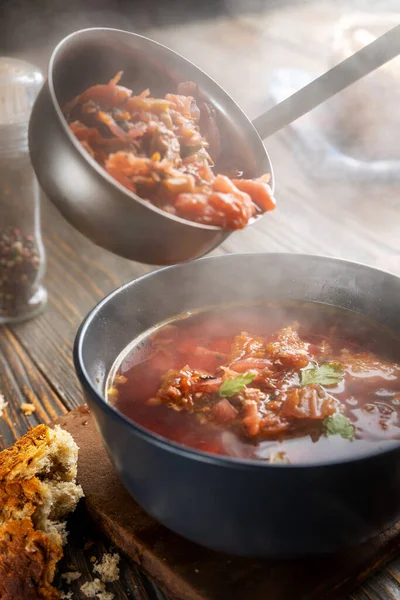 Borsch bir kepçeden bir kaseye dökülüyor, buhar, geleneksel bir Ukrayna sebze çorbası pancar, havuç, domates, patates, lahana, otlar ve sarımsak, yakın çekim derinliği,