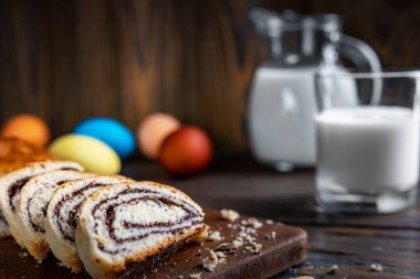Paskalya pastası, ahşap bir masanın üzerinde, sade bir şekilde, seçici odak, sığ alan derinliği, düşük aydınlatma, arka planda bir bardak süt ve renkli yumurta..