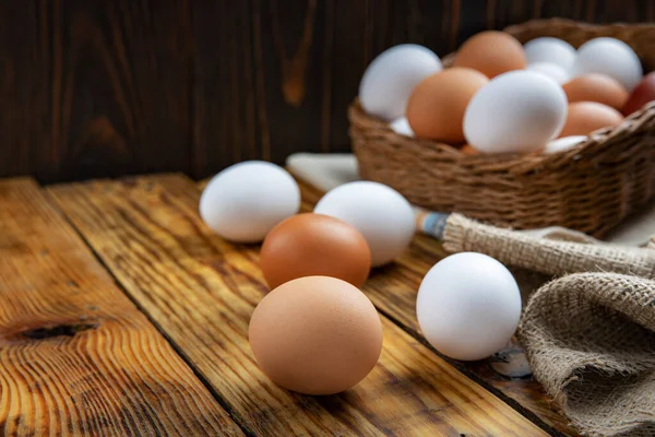 Çiftlik yumurtaları beyaz ve kahverengi, tahta bir masanın üzerinde ve sepetin içinde, yakın plan, düşük ışık, seçici odak, sığ alan derinliği. Organik gıda konsepti