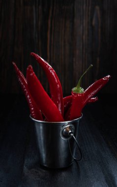 Metal kovada kırmızı biber, kırsal tarzda, koyu ahşap tahtalar, aydınlatılmış ay ışığı, yakın çekim, sığ alan derinliği, seçici odaklanma. Organik gıda konsepti.