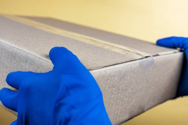 Eldivenli kurye, sarı stüdyo arka planında boş bir karton kutu tutuyor. Yakın plan, sığ alan derinliği, seçici odaklanma. Coronavirus servisi. Çevrimiçi mağaza, yemek teslimatı