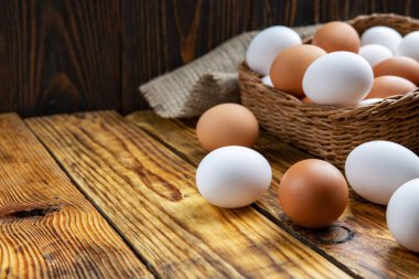 Çiftlik yumurtaları beyaz ve kahverengi, tahta bir masanın üzerinde ve sepetin içinde, yakın plan, düşük ışık, seçici odak, sığ alan derinliği. Organik gıda konsepti