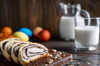Paskalya pastası, ahşap bir masanın üzerinde, sade bir şekilde, seçici odak, sığ alan derinliği, düşük aydınlatma, arka planda bir bardak süt ve renkli yumurta..