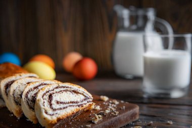 Paskalya pastası, ahşap bir masanın üzerinde, sade bir şekilde, seçici odak, sığ alan derinliği, düşük aydınlatma, arka planda bir bardak süt ve renkli yumurta..