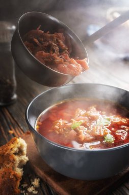 Borsch bir kepçeden bir kaseye dökülüyor, buhar, geleneksel bir Ukrayna sebze çorbası pancar, havuç, domates, patates, lahana, otlar ve sarımsak, yakın çekim derinliği,
